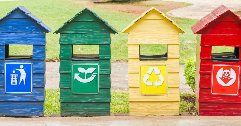 Blue, green, yellow and red bins on stand near footpath.